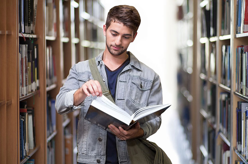 Schüler steht in der Bibliothek in einem Buch blätternd